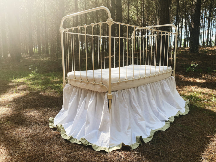 White gathered crib skirt with sage ruffle trim on iron crib, full front view outdoors, 22 inch drop farmhouse nursery