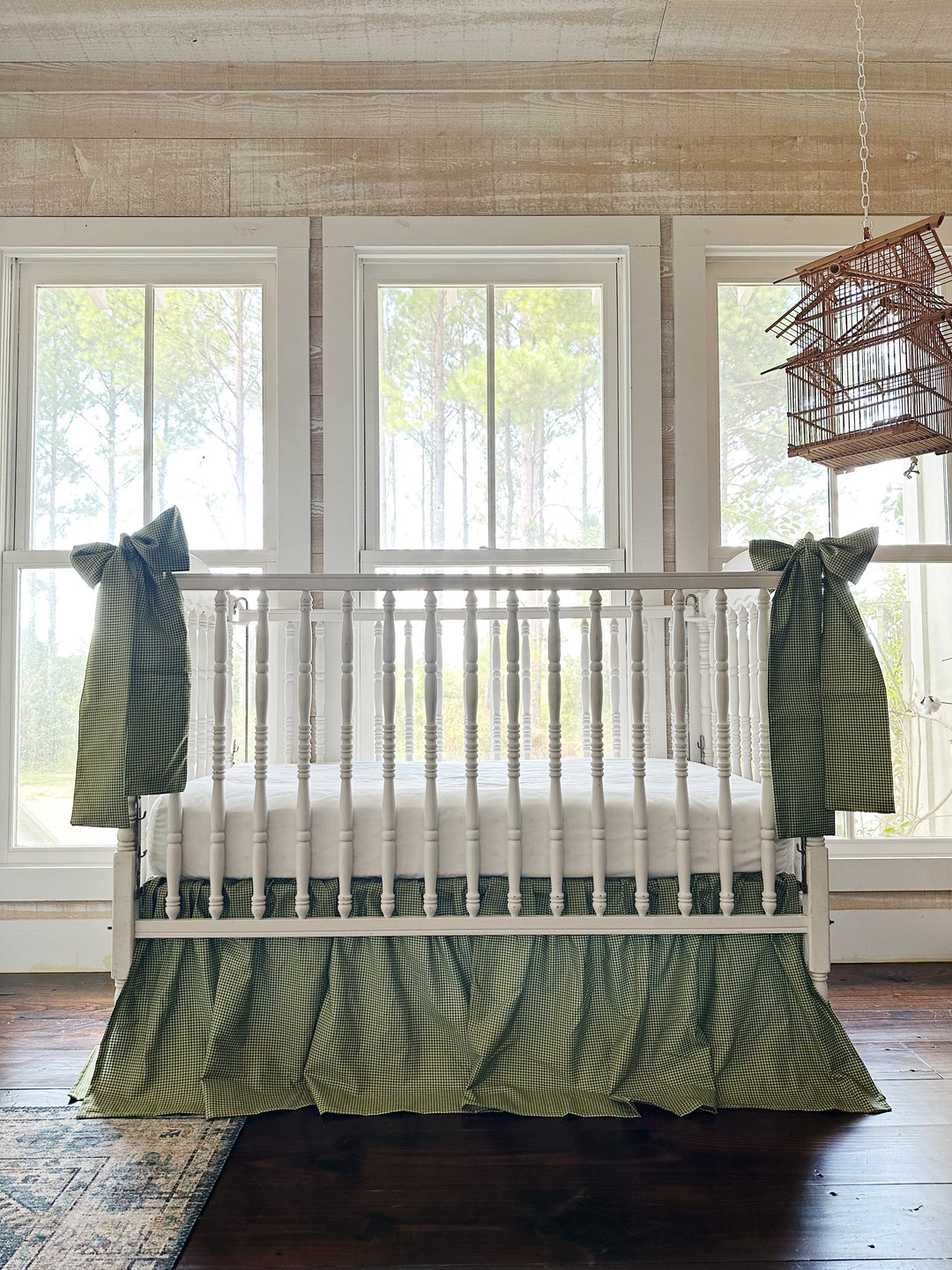 Green gingham crib skirt and two crib bow sashes on a white spindle crib in a farmhouse nursery