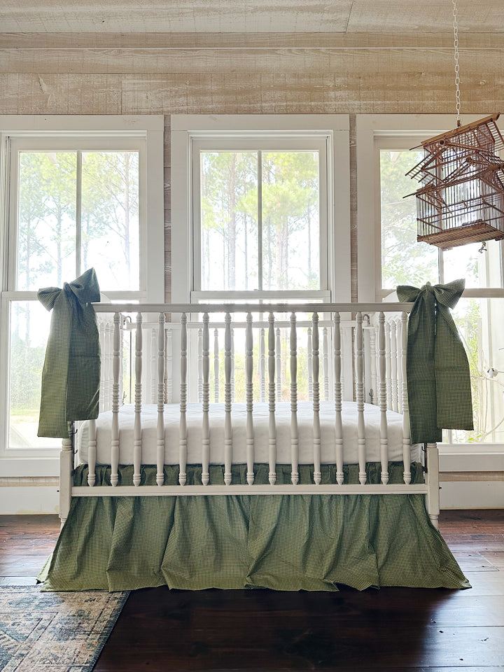 Green gingham crib skirt and two crib bow sashes on a white spindle crib in a farmhouse nursery