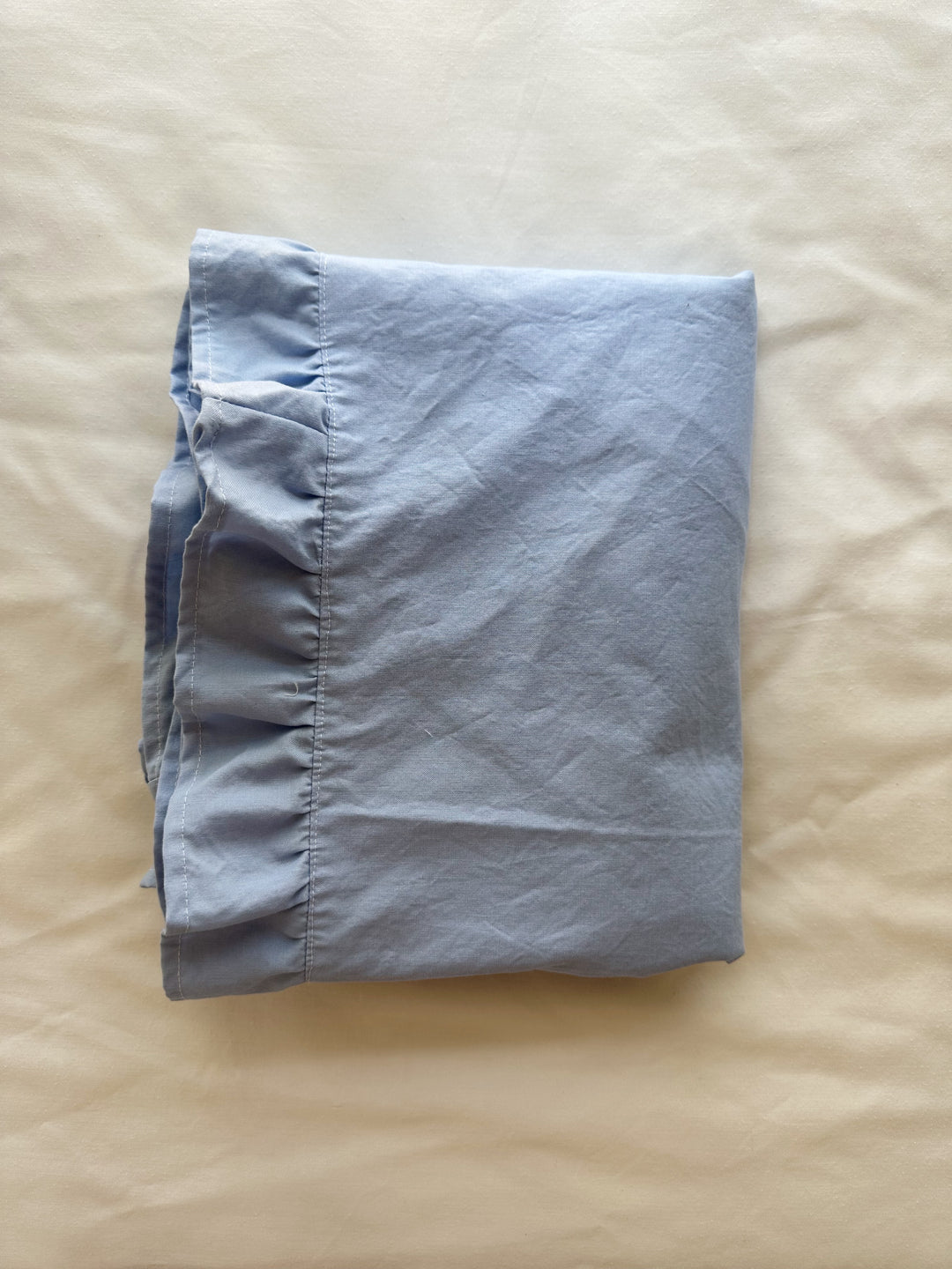 Baby blue ruffled crib blanket folded on cream linen, showing the ruffle border and hem - High Cotton Textile
