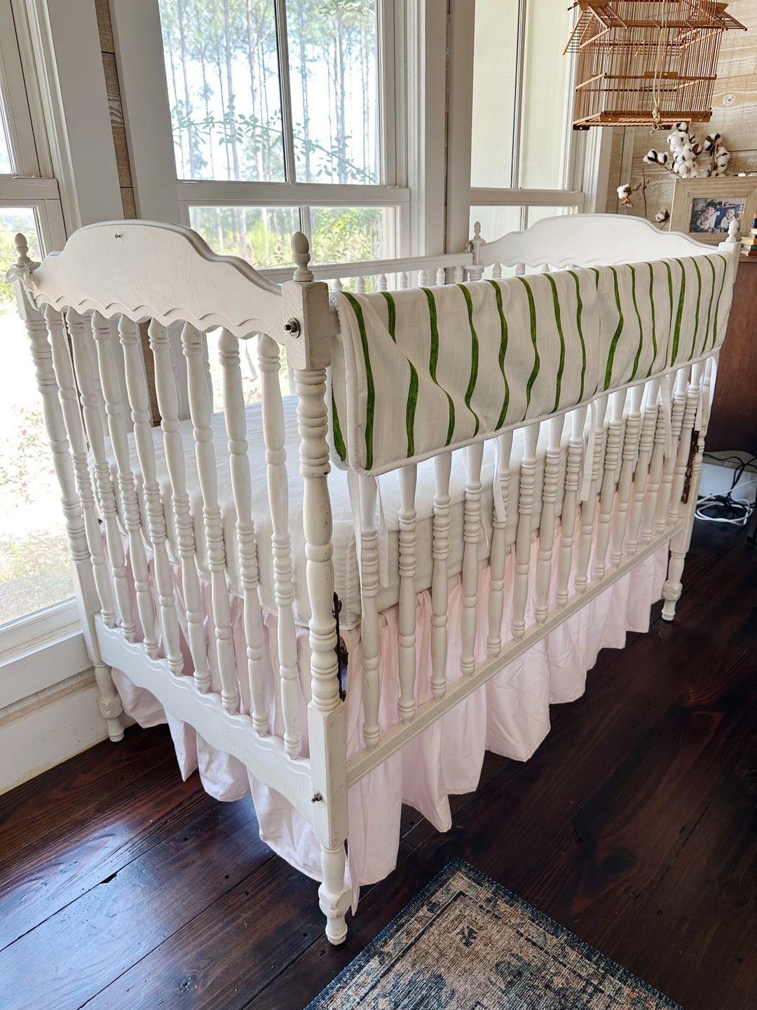 Angled view of the striped rail cover and the soft pink skirt gathering below the spindles