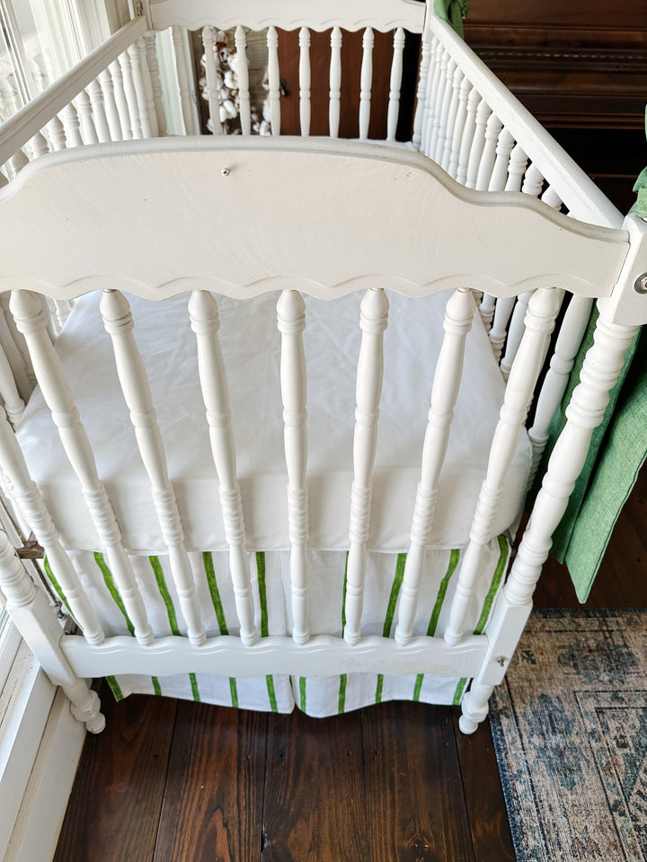 Looking down at the head of the crib, white sheet above the green striped skirt