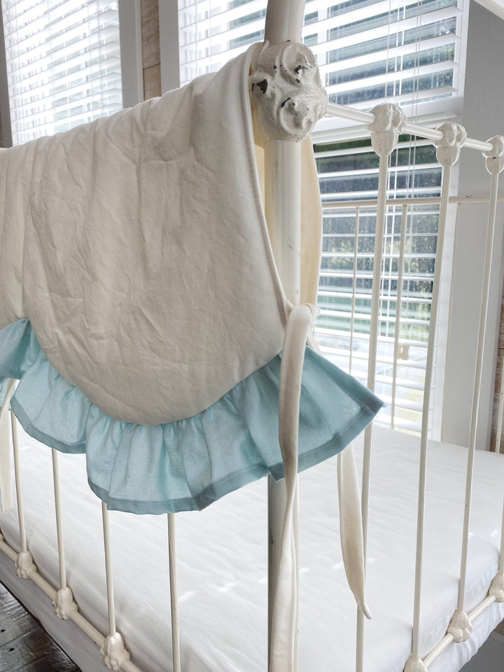 Close-up of a scalloped curve edged in mist blue ruffle with ivory cotton ties on a crib rail
