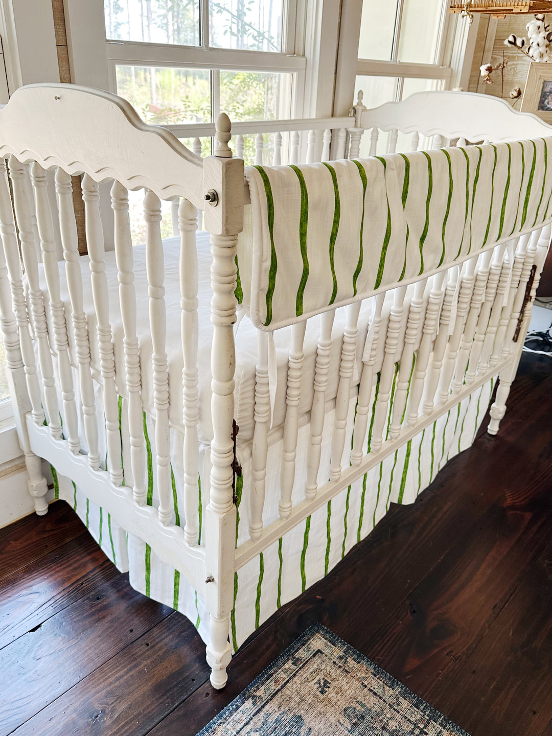 Angled view from the head of the crib, the stripe running the length of the long rail and down the skirt