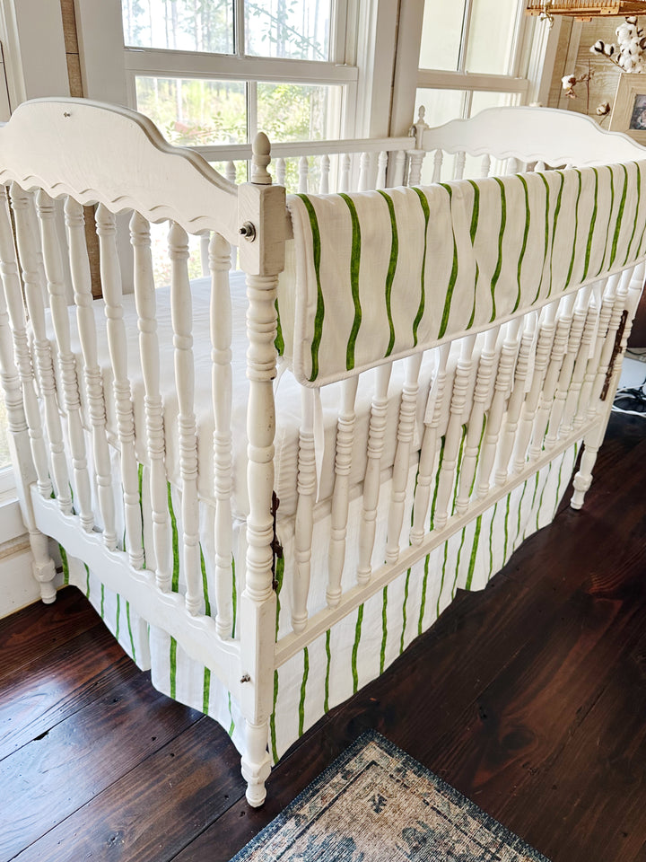 Angled view from the head of the crib, the stripe running the length of the long rail and down the skirt