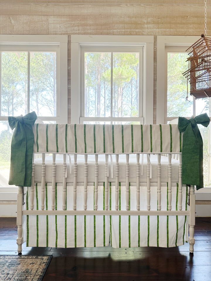 Green and white striped tailored crib rail cover and matching striped skirt with two cypress green bows on a white spindle crib