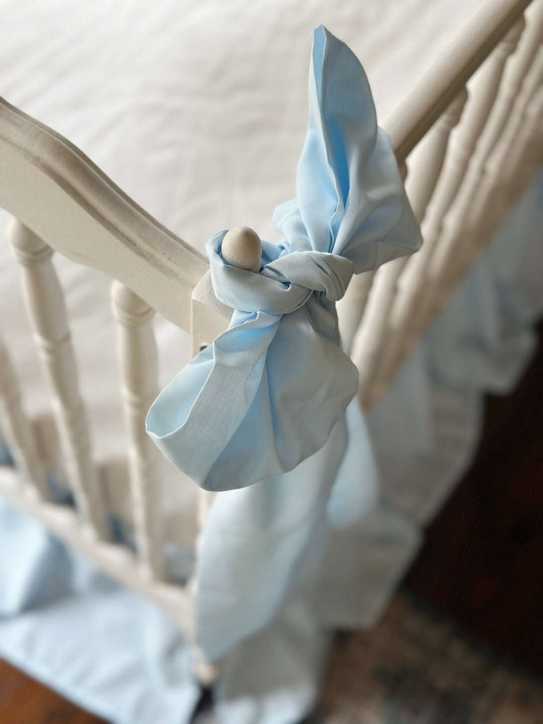 Overhead view of the blue bow knotted around the crib's turned wooden finial