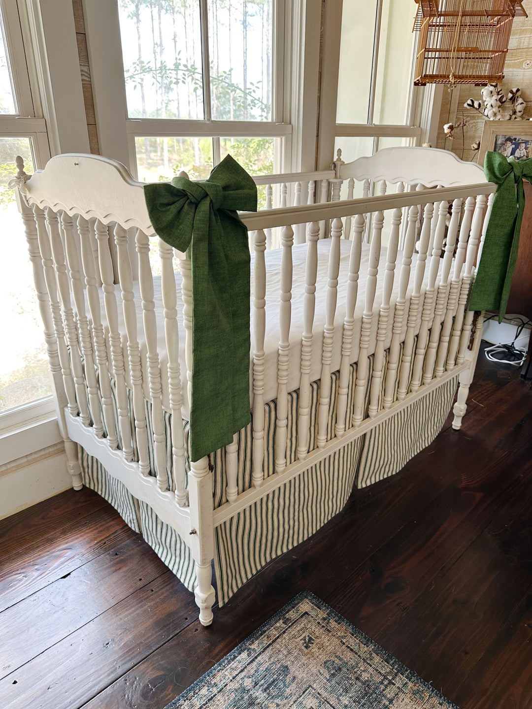Pine green ticking tailored crib skirt with two solid cypress green sashes tied to the crib posts