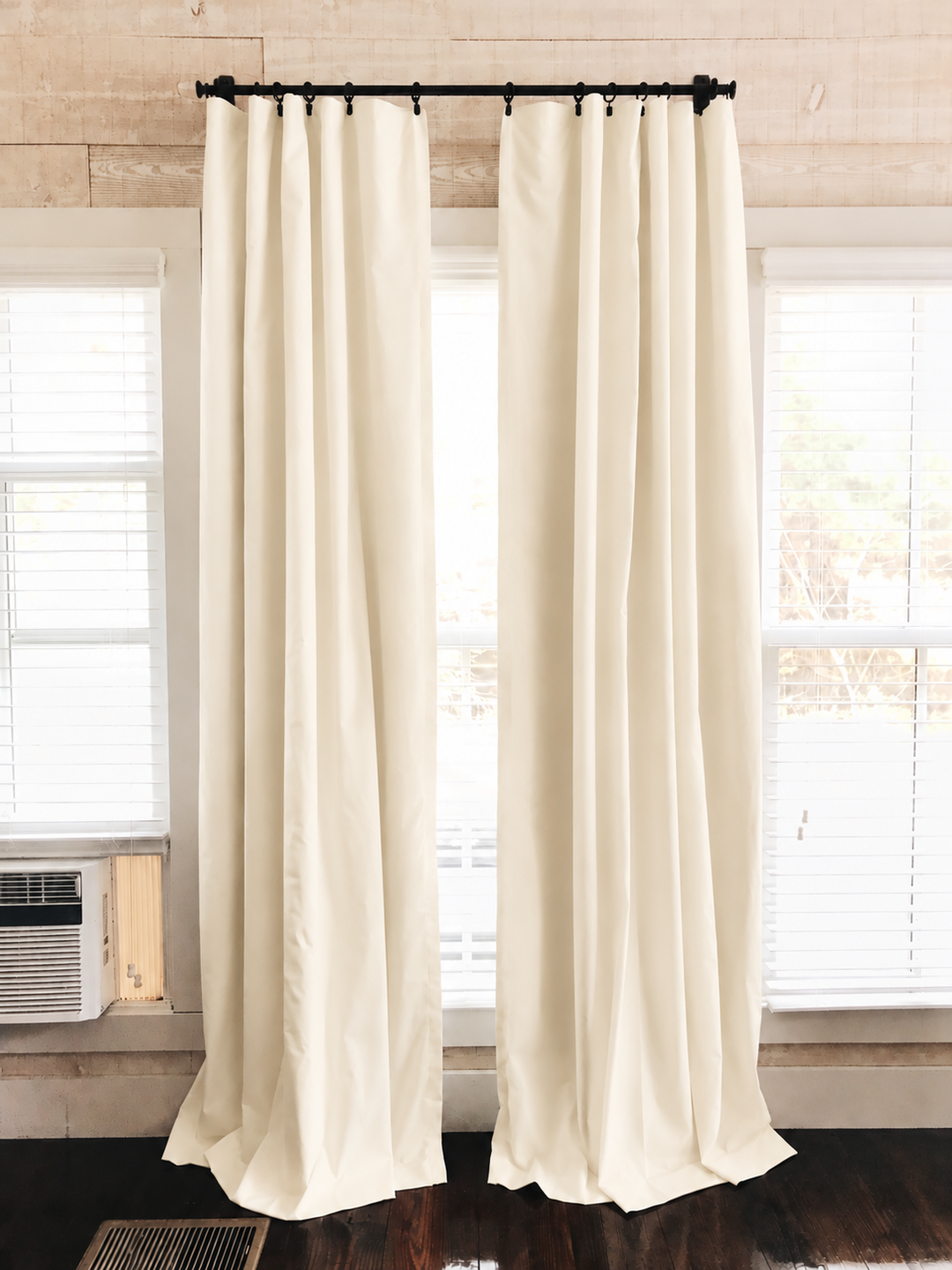 Ivory blackout curtains pulled open either side of a bright window, pooling slightly on dark floorboards