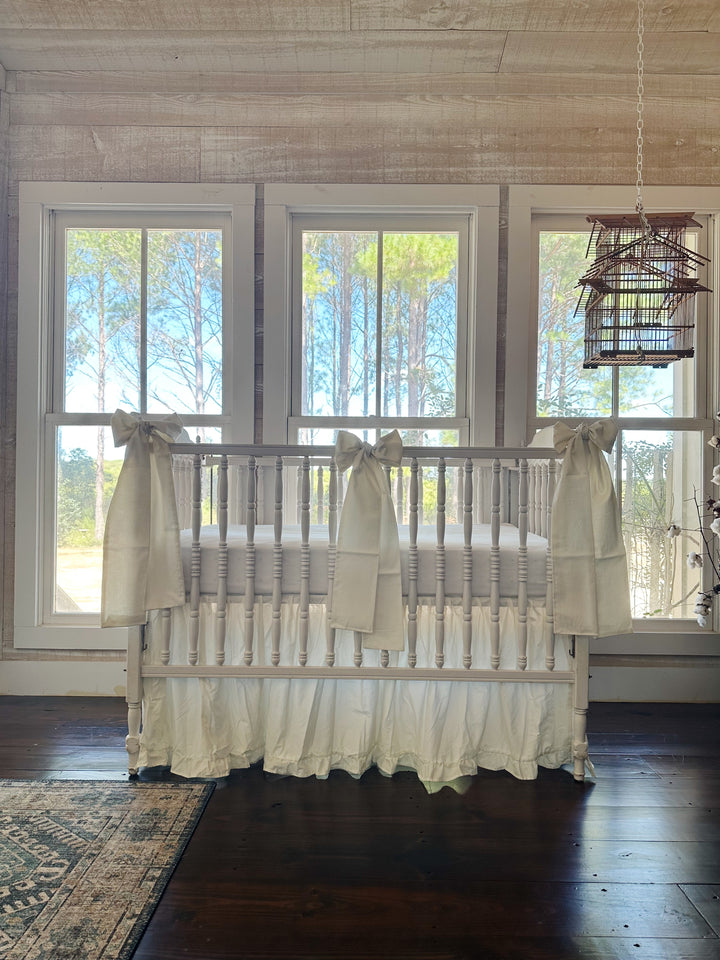 Nursery with shiplap walls and a hanging birdcage, white spindle crib dressed in a porcelain ruffled skirt with bows at both corners and center