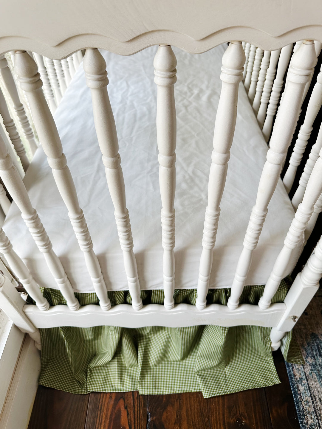 Overhead view of a white spindle crib with the green gingham farmhouse crib skirt