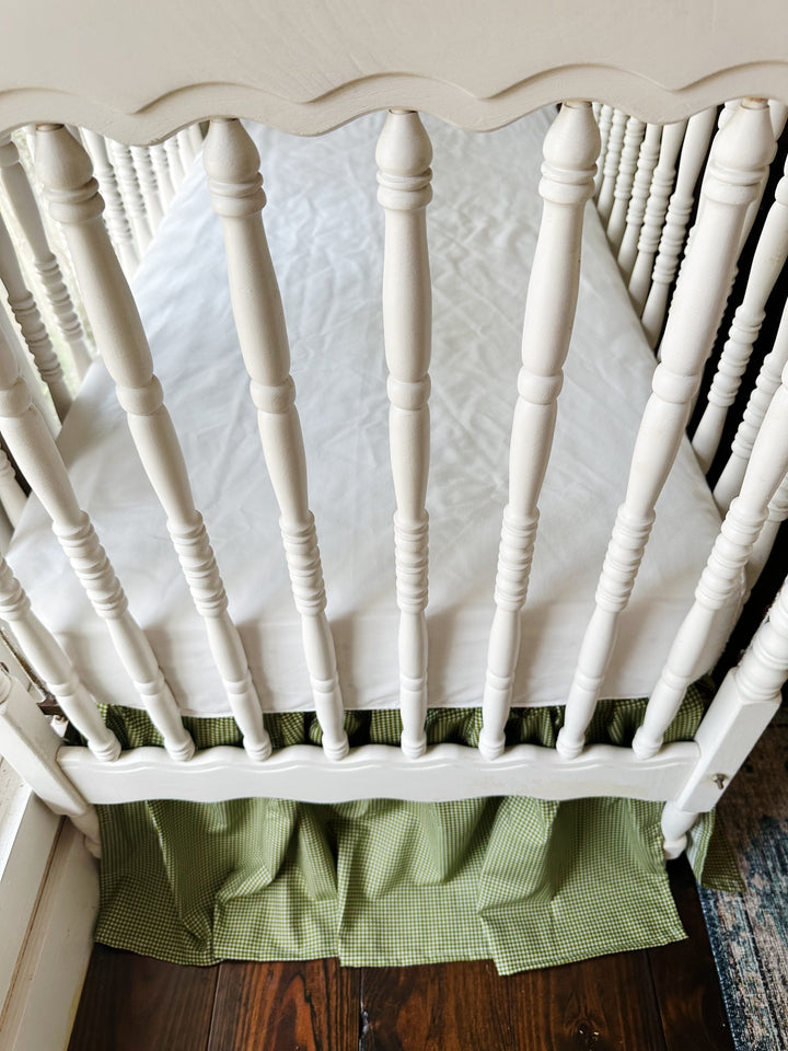 Overhead view of a white spindle crib with the green gingham farmhouse crib skirt