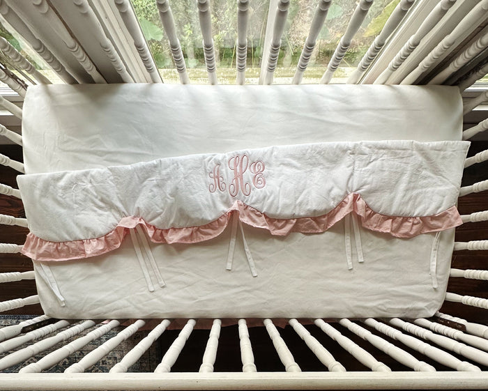 White and Sisters Pink scalloped crib rail cover laid flat, showing its full length, pink ruffle and white cotton ties