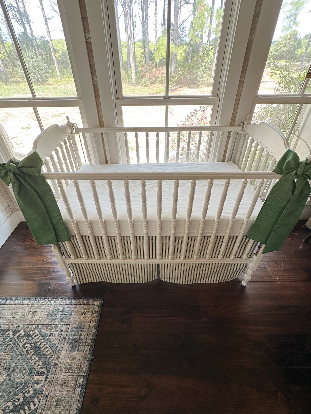 Looking slightly down at the crib, both sashes hanging long against the ticking skirt