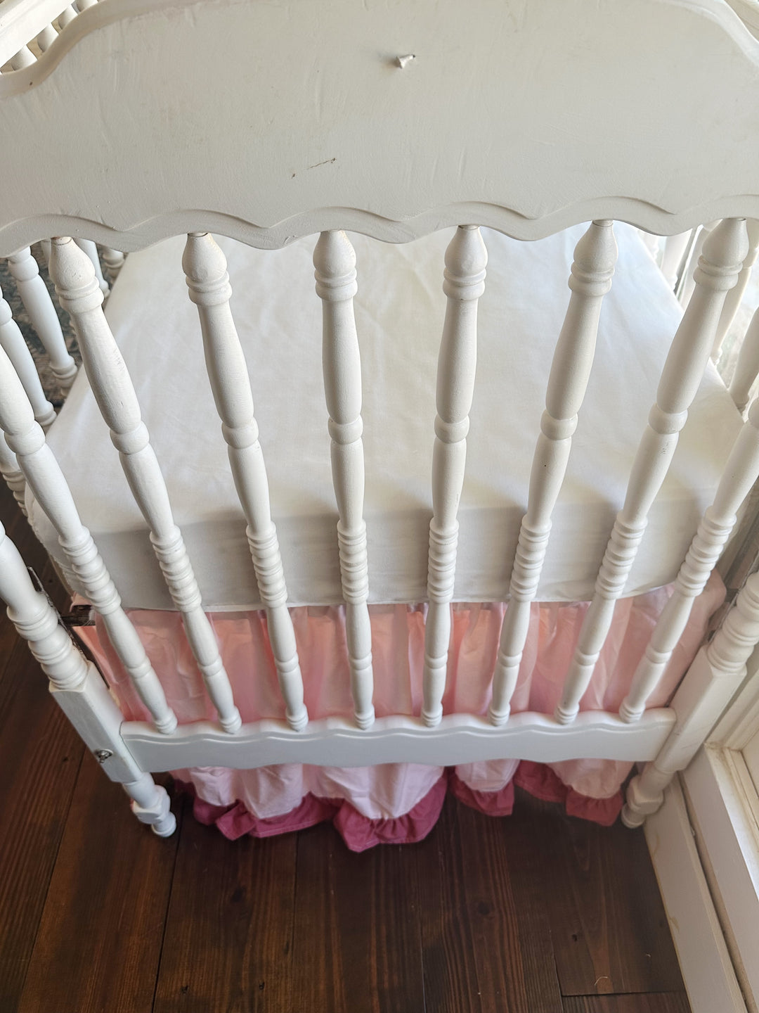Looking down over the scalloped footboard at the white mattress, with the Sisters Pink skirt and blush ruffle beneath