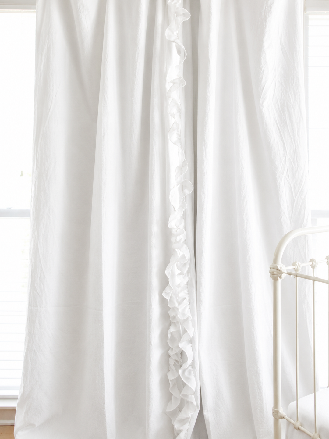 White ruffled blackout nursery curtains hanging beside a white crib, ruffle running down the leading edge of each panel - High Cotton Textile