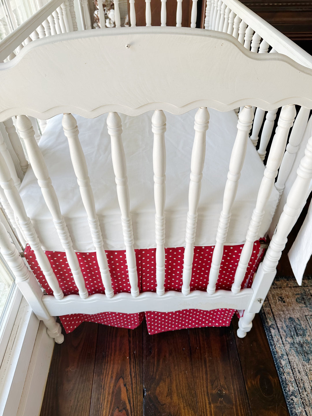 Seen from the end of the crib, the pleated dotted skirt beneath a plain white sheet