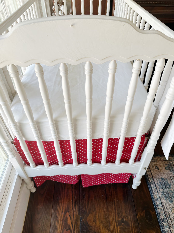 Seen from the end of the crib, the pleated dotted skirt beneath a plain white sheet