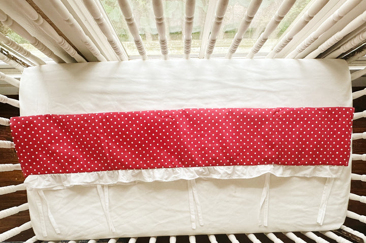 Overhead view of the rail cover folded over the crib rail, showing the plain white back panel