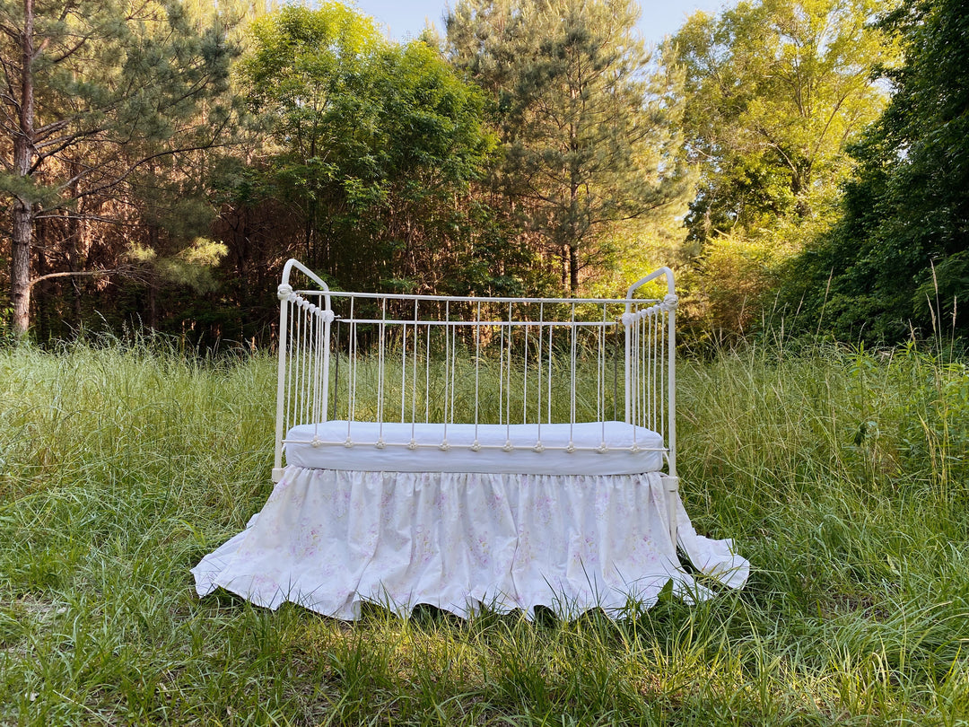 Lavender shabby chic floral crib skirt on white iron crib, golden hour outdoor photo