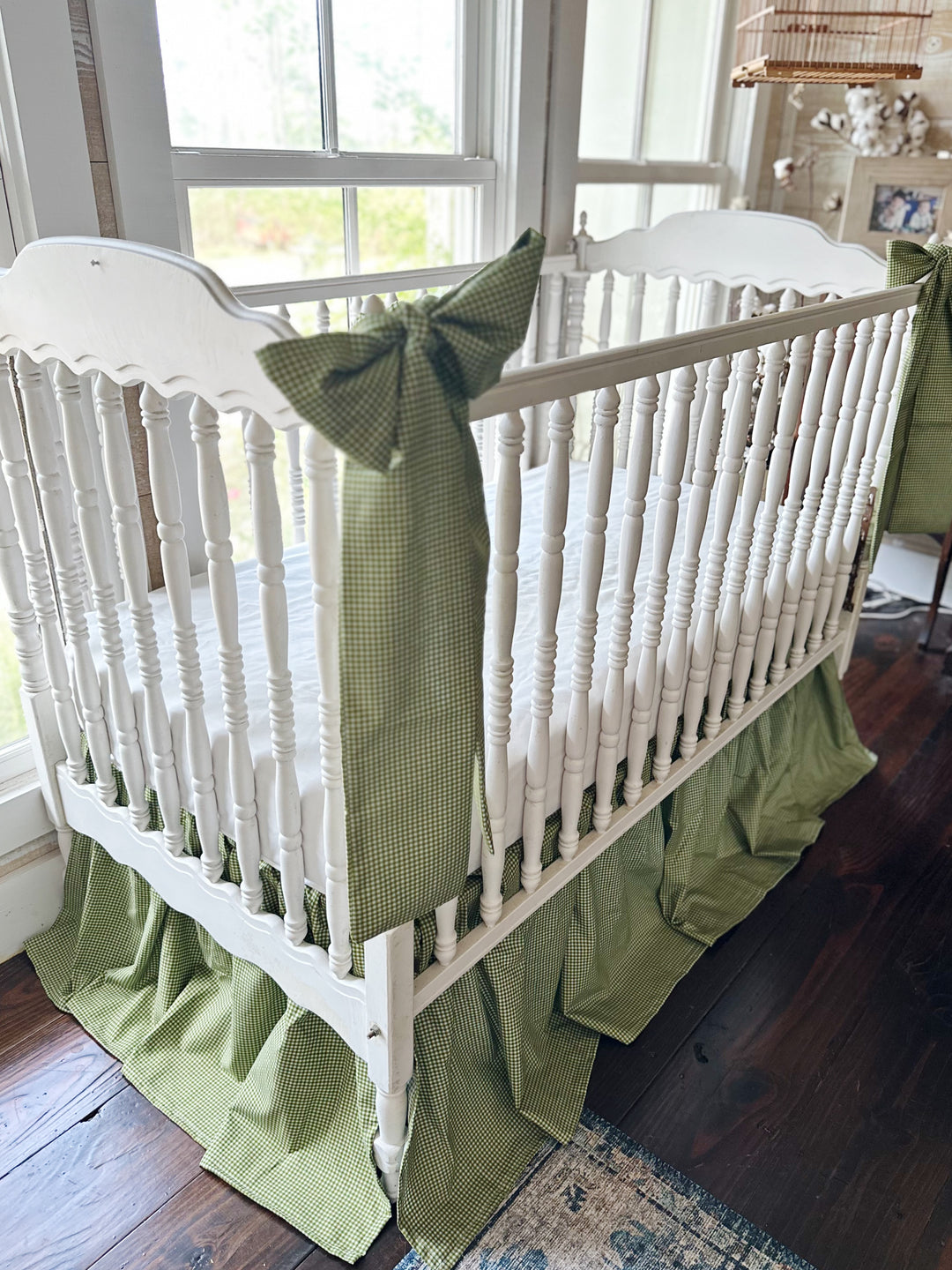 Angled view of the pine green gingham crib skirt with a long bow sash draped over the crib rail
