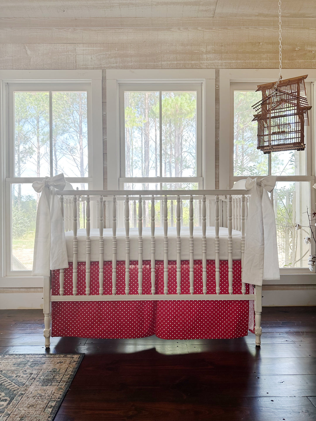The dotted skirt and white sashes in a pine-paneled room with three windows and a hanging birdcage