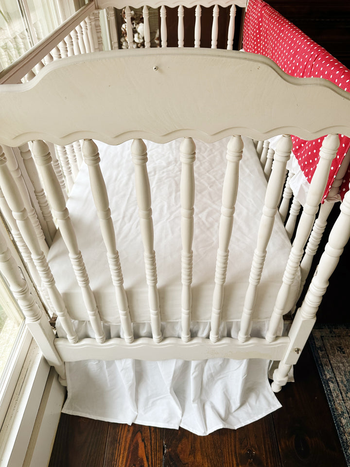 Looking down past the scalloped headboard at the white sheet and gathered white skirt