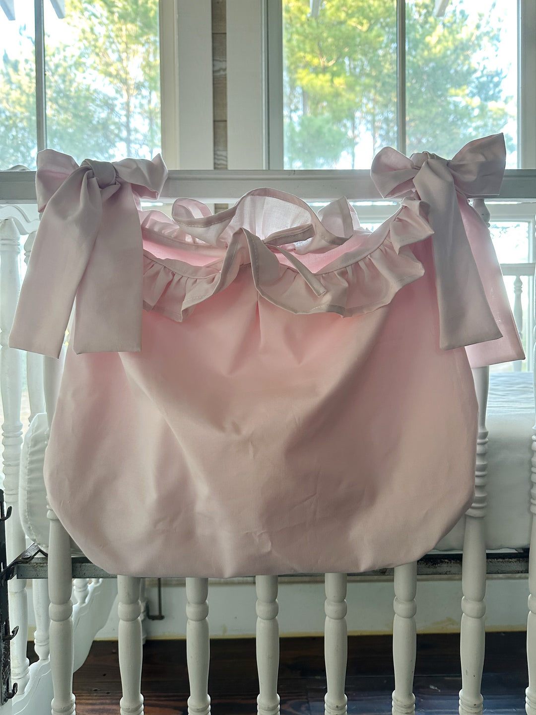 Baby pink ruffled hanging crib caddy tied to a white crib rail with two big pink sash bows