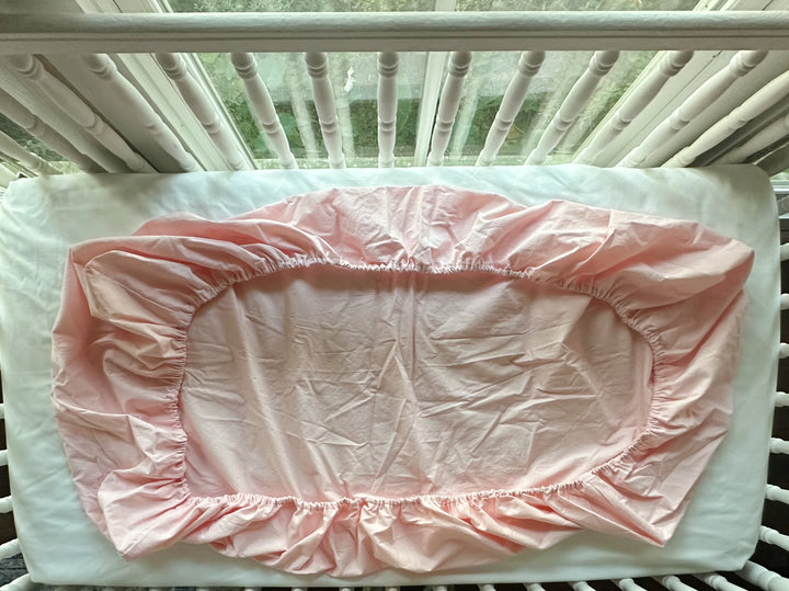Underside of the Sisters Pink fitted crib sheet laid flat, showing elastic gathered all the way around