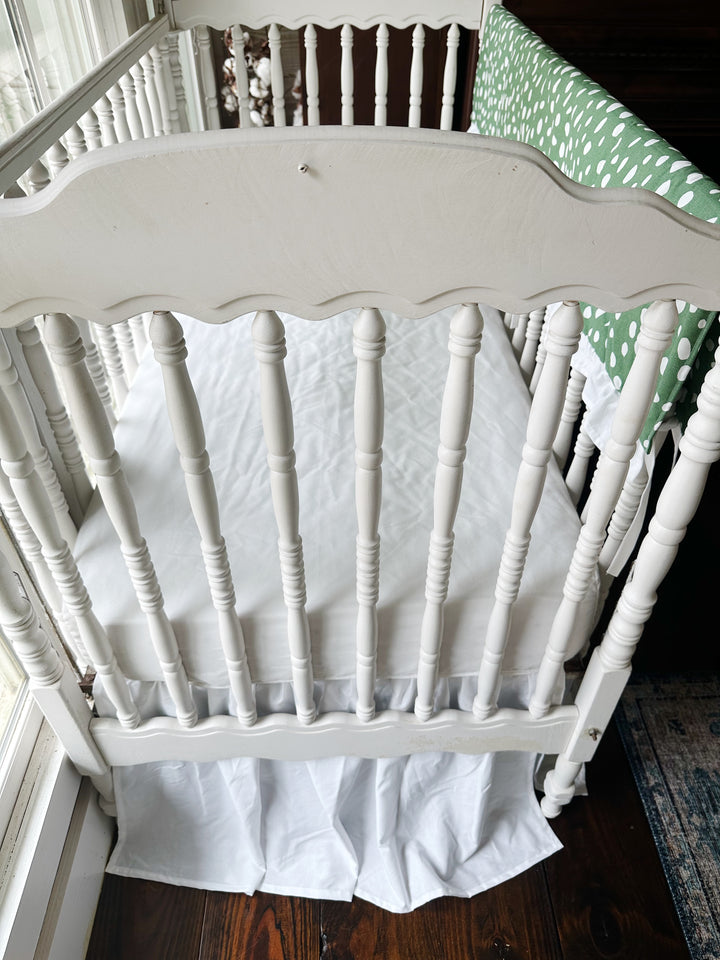 Looking down past the scalloped headboard at the white sheet and gathered white skirt