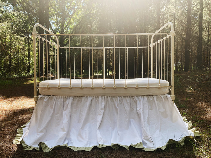 Overhead close-up of white gathered crib skirt with sage green ruffle trim on iron crib, two-tone heirloom nursery bedding