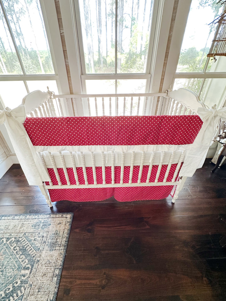 Cherry red and white polka dot ruffled crib rail cover with a matching dotted tailored skirt and two white bows