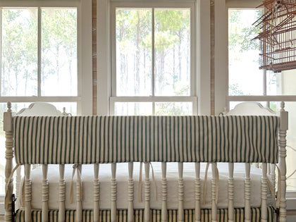 Pine green ticking simple crib rail cover across the long rail of a white spindle crib, natural ties hanging below