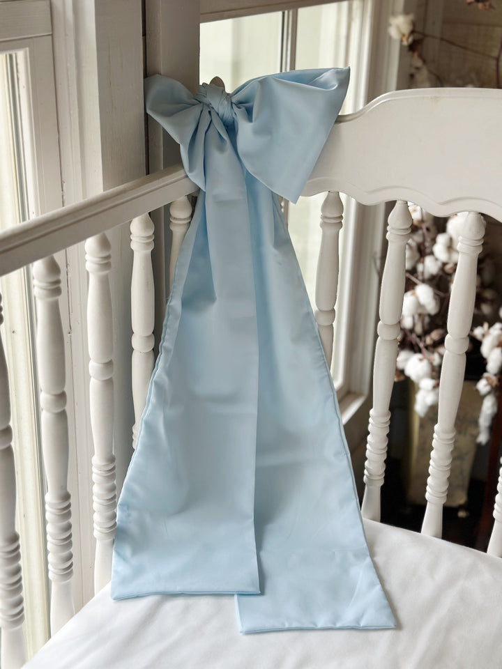 Heirloom blue crib bow tied to a white spindle crib rail with long tails falling below