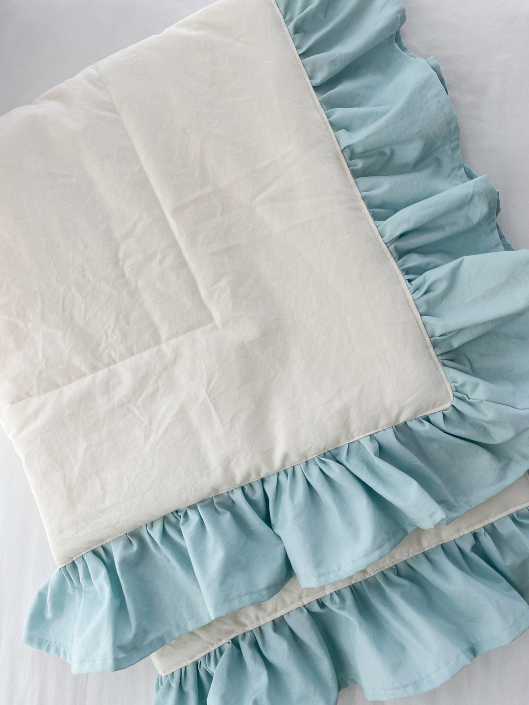Flat detail of the ivory quilt panel and its double gathered mist blue cotton ruffle