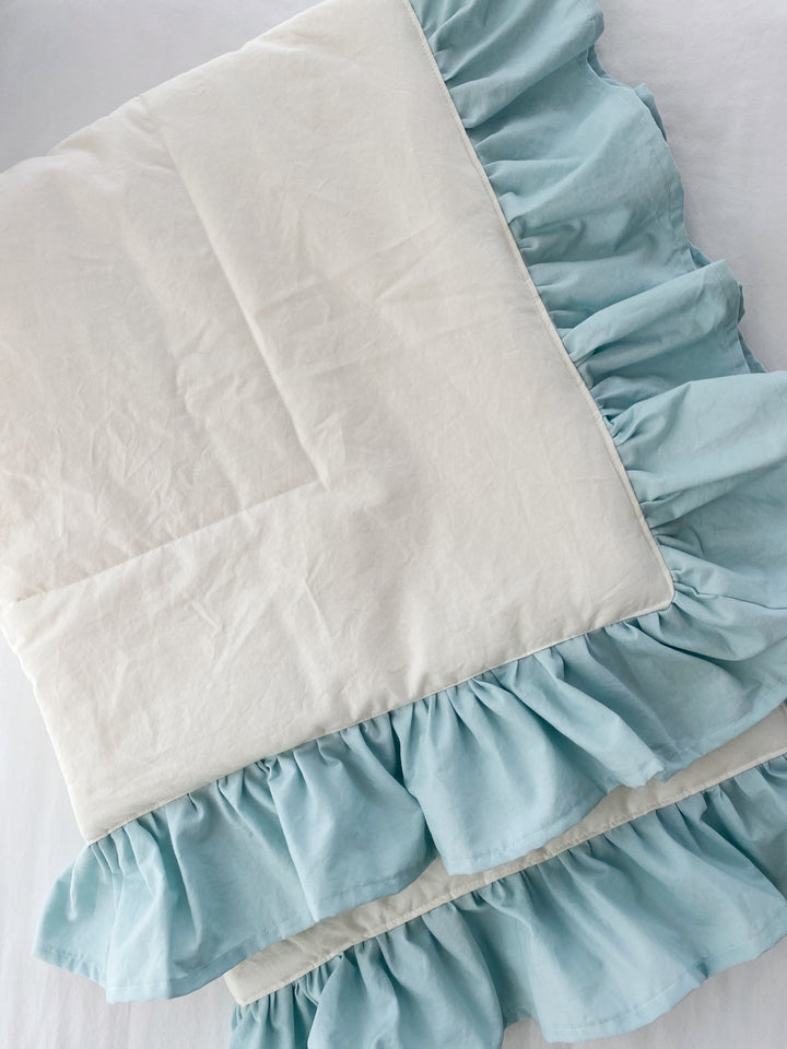 Flat detail of the ivory quilt panel and its double gathered mist blue cotton ruffle