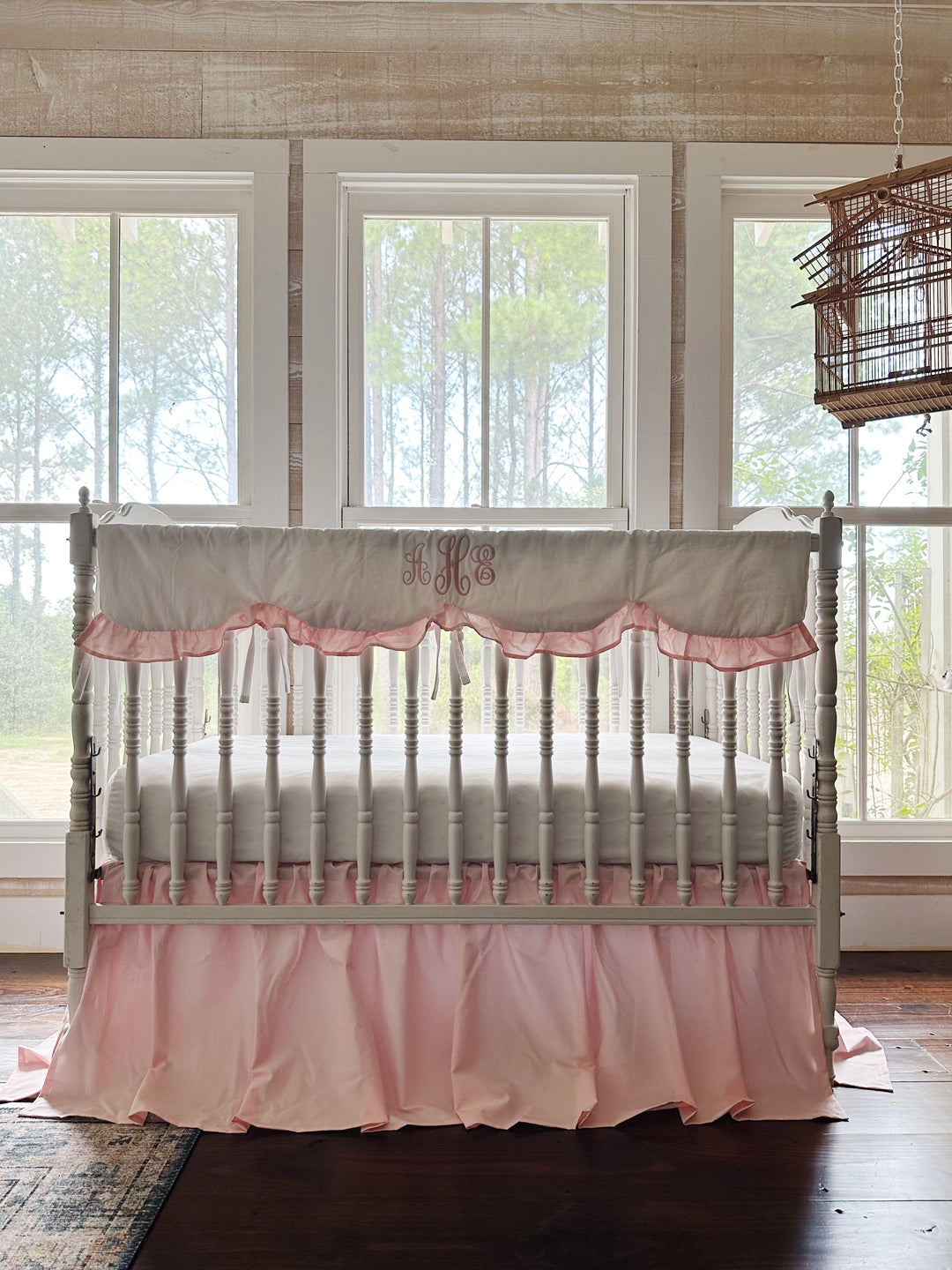 White spindle crib styled with a Sisters Pink scalloped rail cover and farmhouse crib skirt in a bright farmhouse nursery