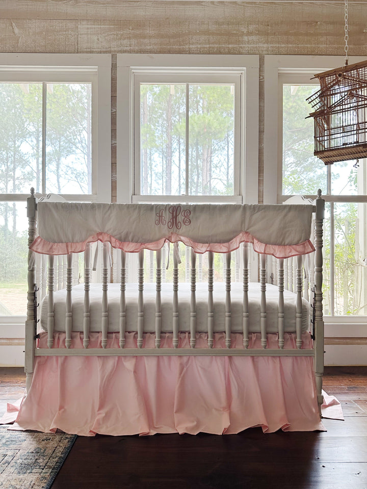 White spindle crib styled with a Sisters Pink scalloped rail cover and farmhouse crib skirt in a bright farmhouse nursery