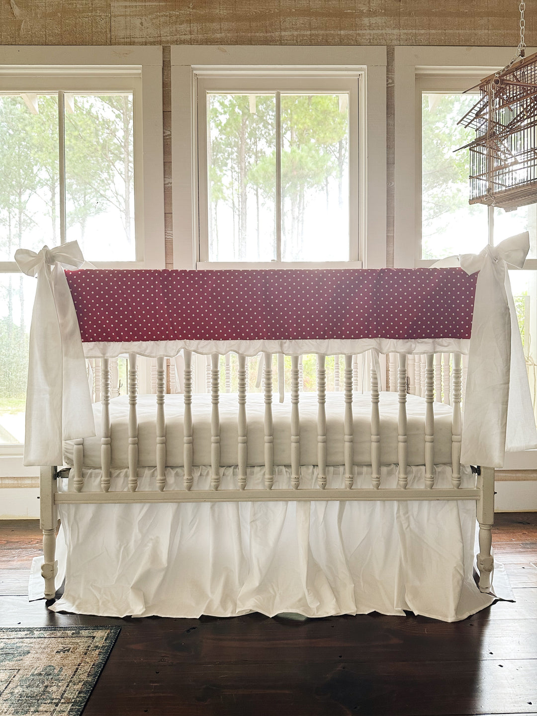 Straight-on view of the red polka dot crib set with both white bows on the front posts