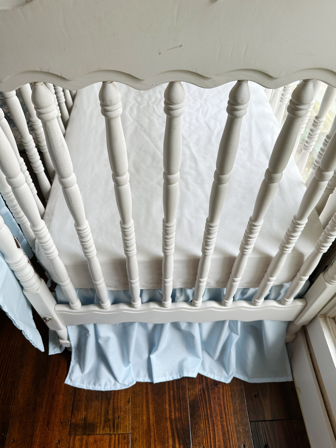 Looking down into the crib from the end where the blue skirt gathers below the mattress