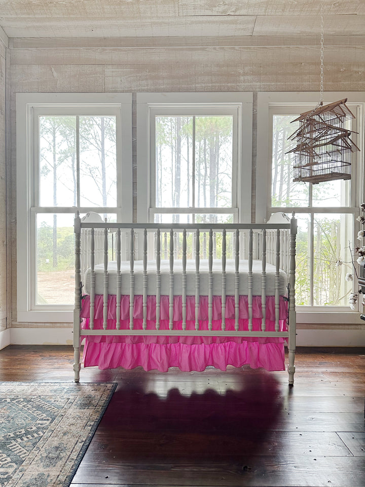 Nursery with whitewashed plank walls and a hanging birdcage, white spindle crib dressed in a pink three-tier ruffled crib skirt