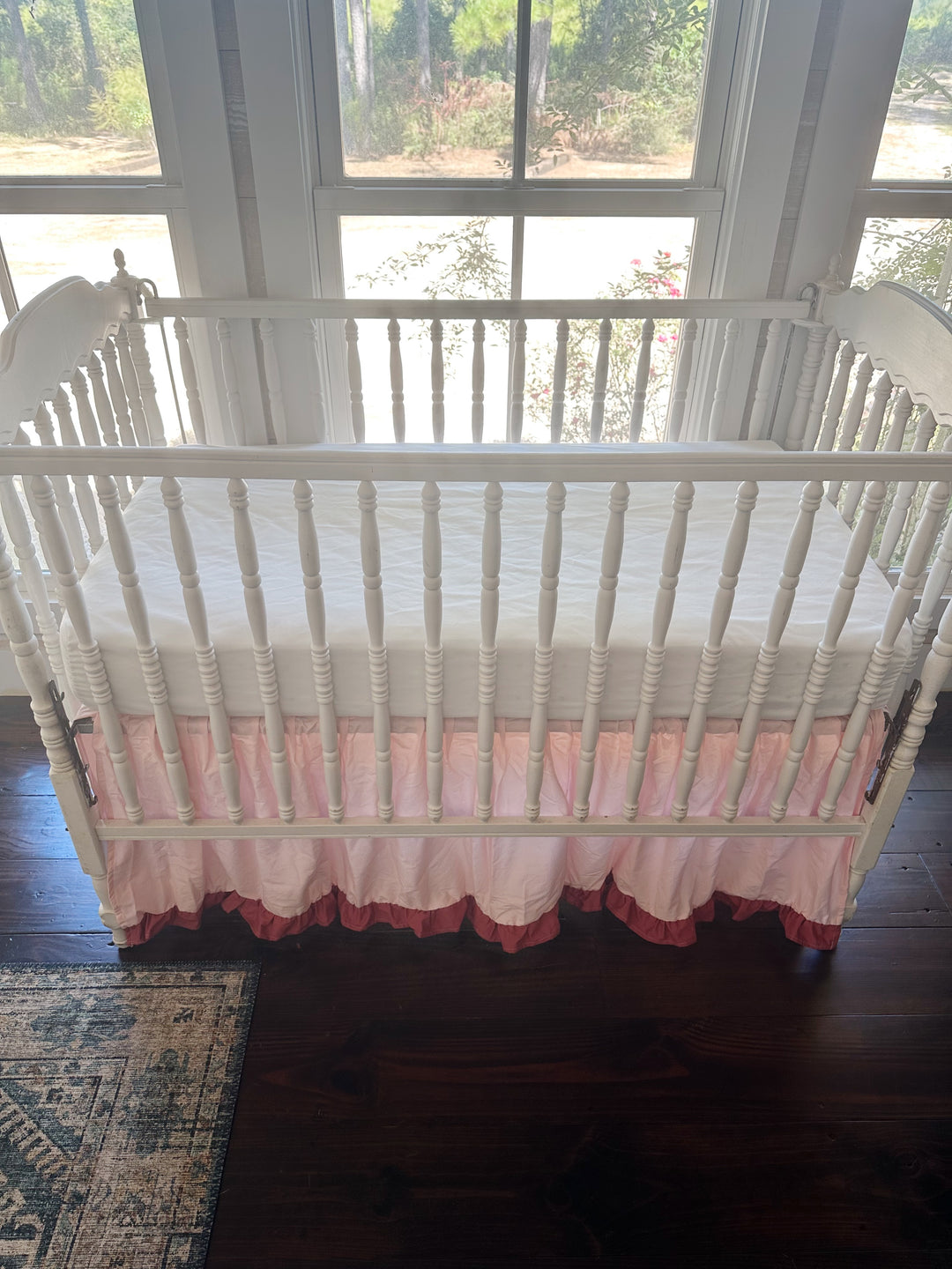 Front of the crib from standing height, white fitted sheet above a Sisters Pink skirt with a blush ruffle