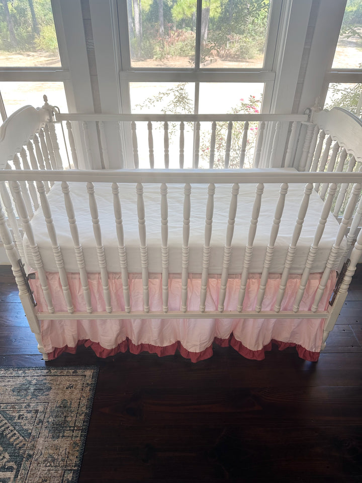 Front of the crib from standing height, white fitted sheet above a Sisters Pink skirt with a blush ruffle