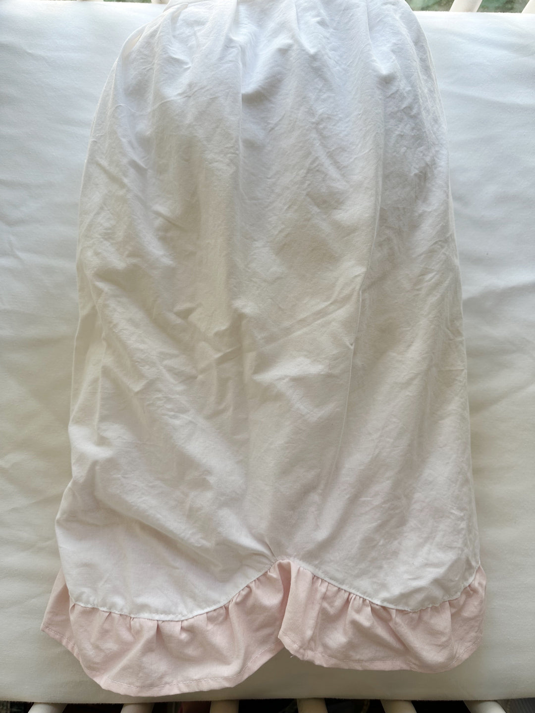 One panel of the crib skirt laid flat over the crib rail showing the scallop shape and pink ruffle edge
