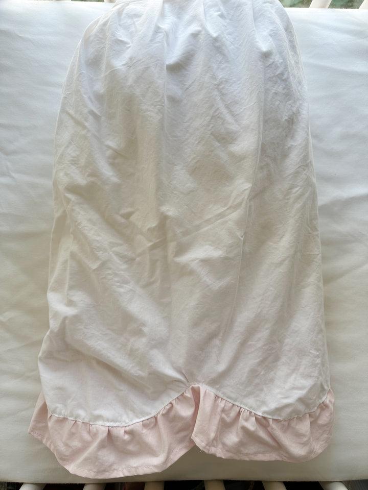 One panel of the crib skirt laid flat over the crib rail showing the scallop shape and pink ruffle edge