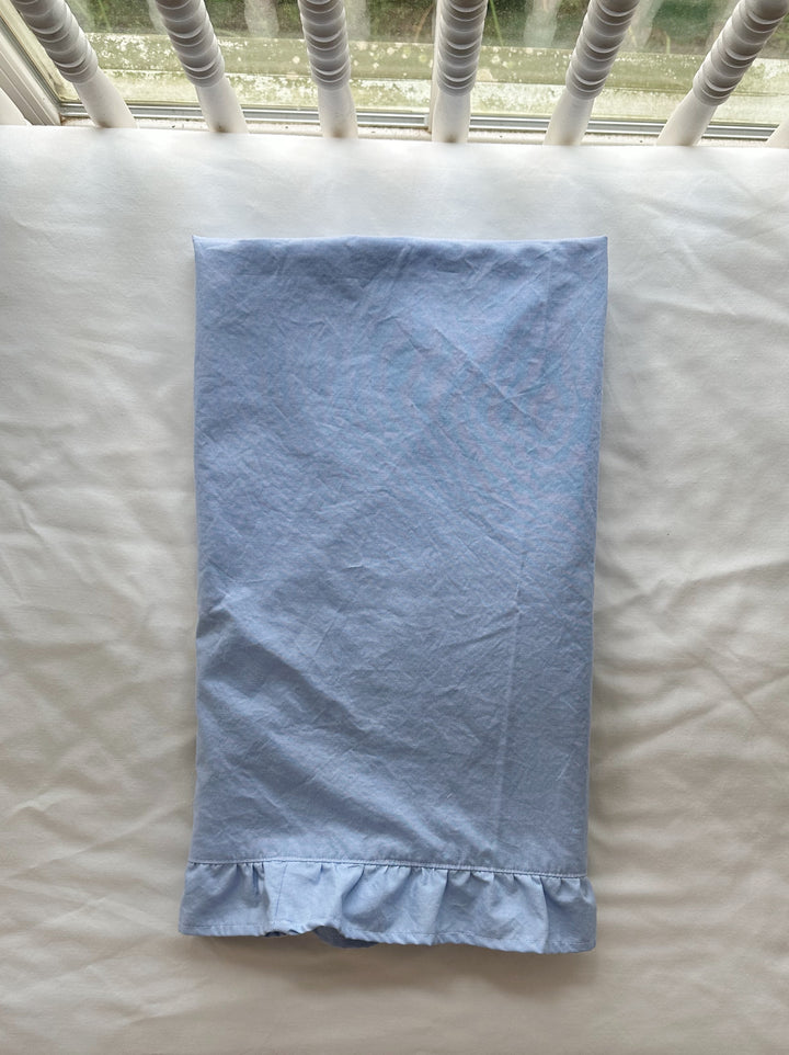 Baby blue ruffled crib blanket folded lengthwise on a white crib mattress with the ruffle at the hem - High Cotton Textile