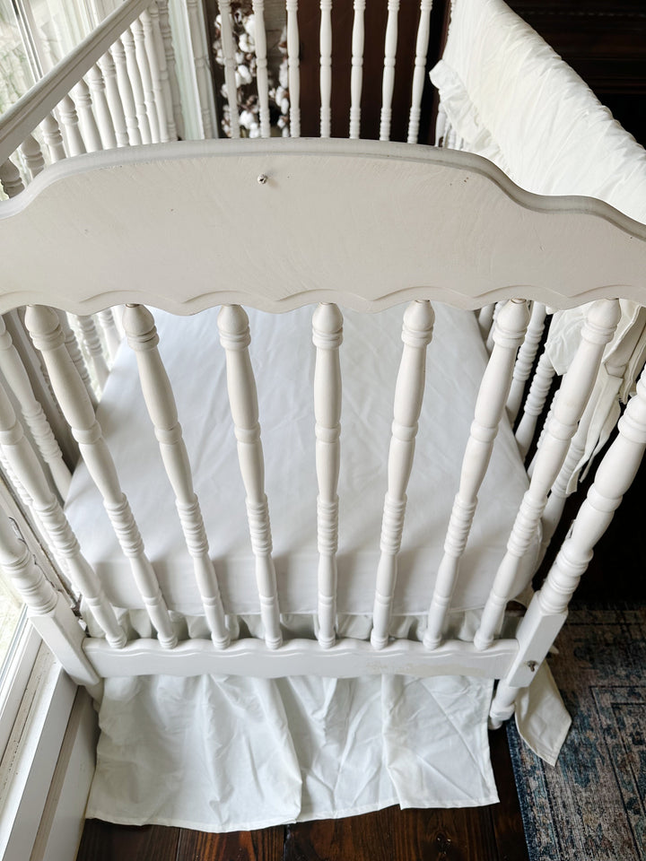 Porcelain crib skirt gathering behind the turned spindles below the mattress line