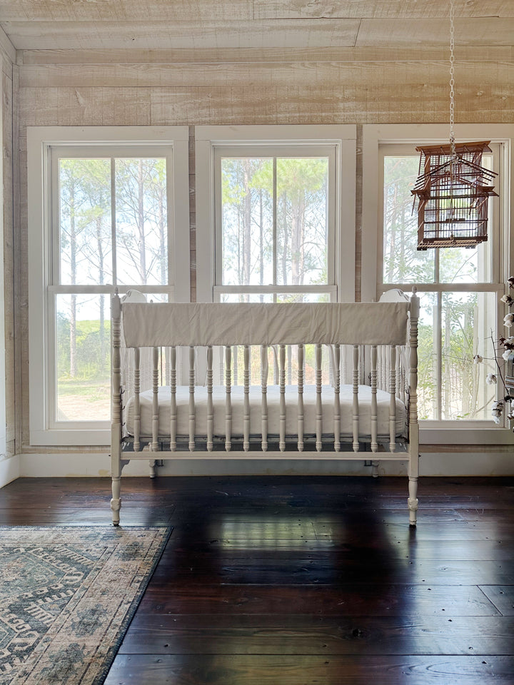 White rail cover without monogram draped across the crib rail beneath three bright windows