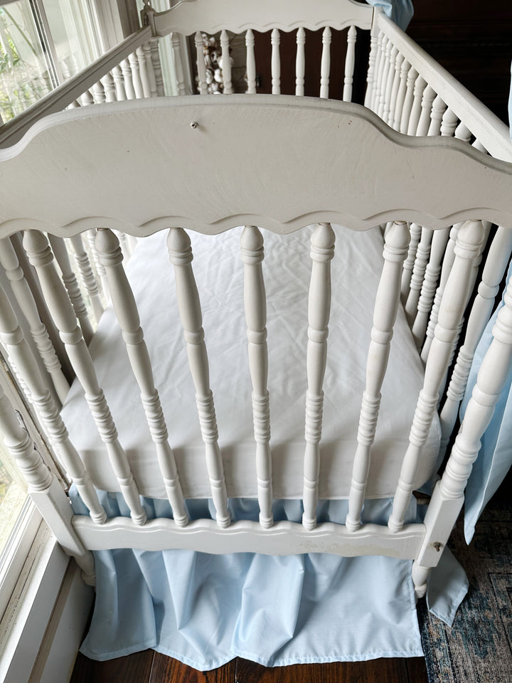 Raised view over the crib with a white fitted sheet above the heirloom blue skirt