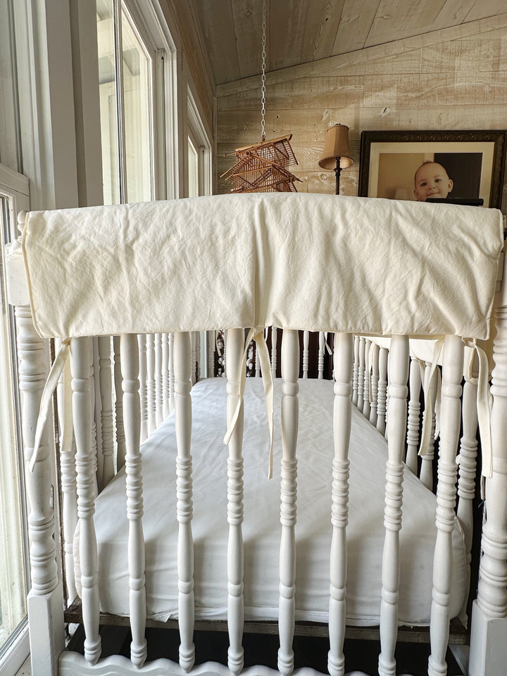 Ivory rail cover across the front of the crib seen from above the mattress